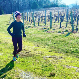 Whitney Heins running in a maroon hat and pants in a vineyard.