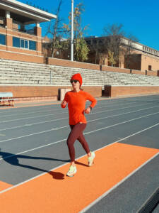 Whitney wearing Tracksmith Bright Baselayer in red running on a track in a red hat.