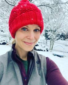 Whitney Heins in a red winter hat and gray winter running vest in the snow.