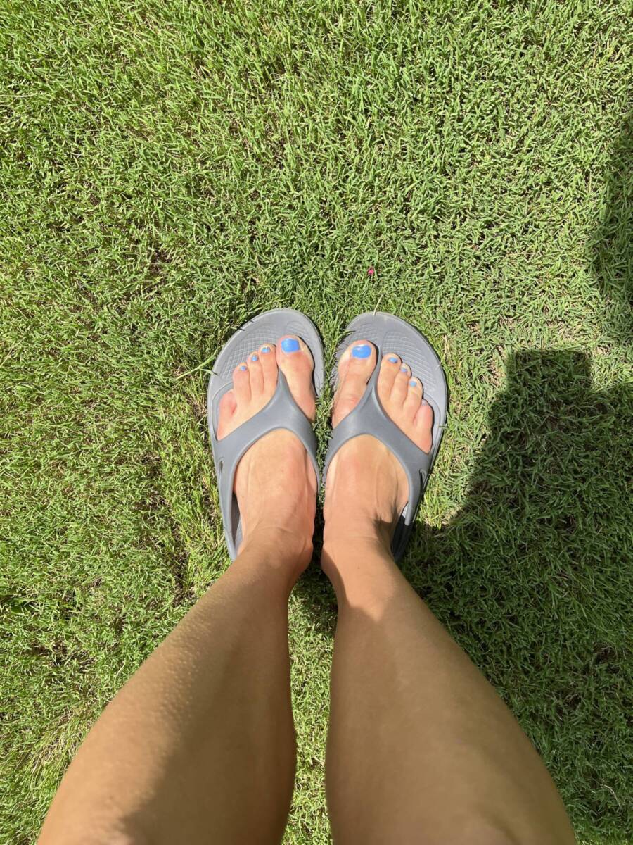 Overhead shot of feet in grey oofos flip flops.