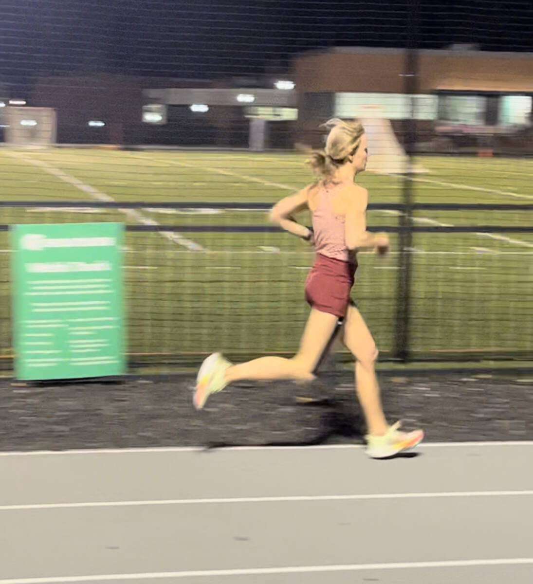 Whitney Heins running on a track in a red top and shorts.