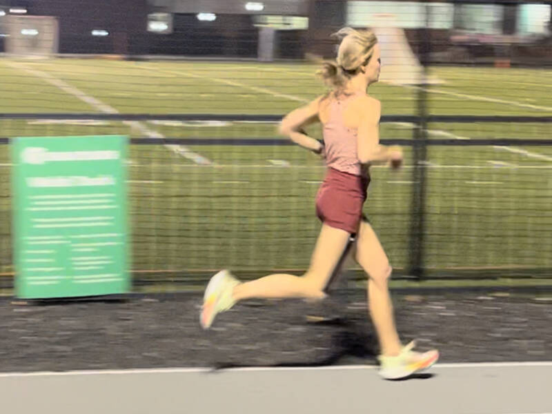 Whitney Heins running on a track in a red top and shorts.