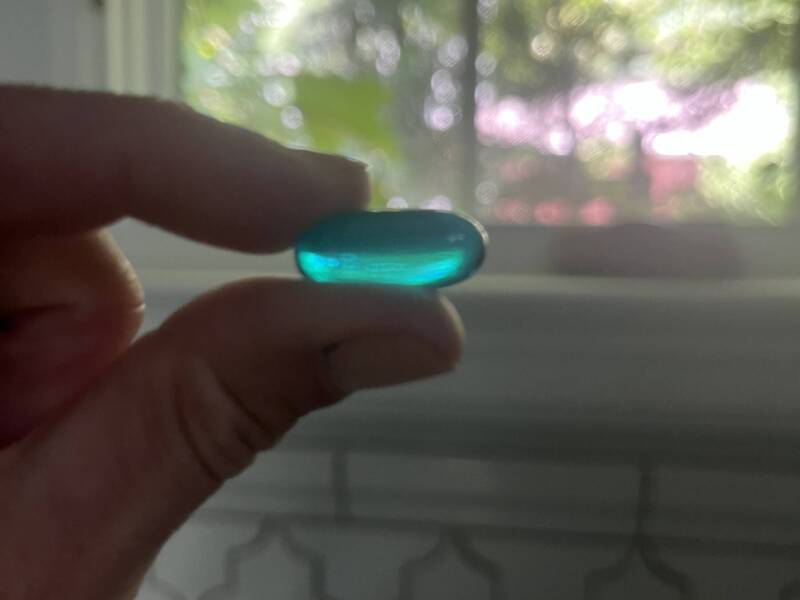 Finger holding blue ibuprofen capsule