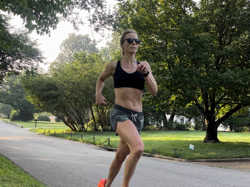 Woman running in orange shoes, black sports bra, and green shorts.