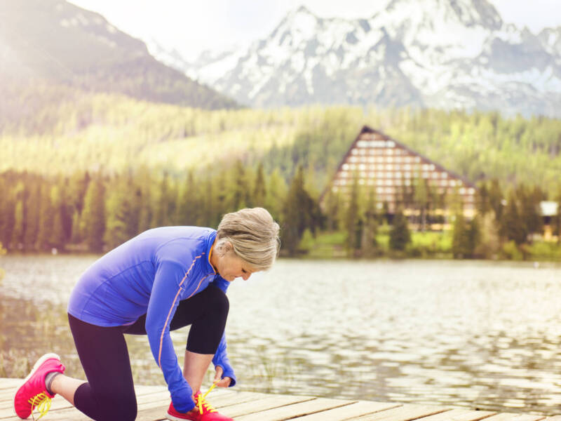 older lady tying running shoe in mountains